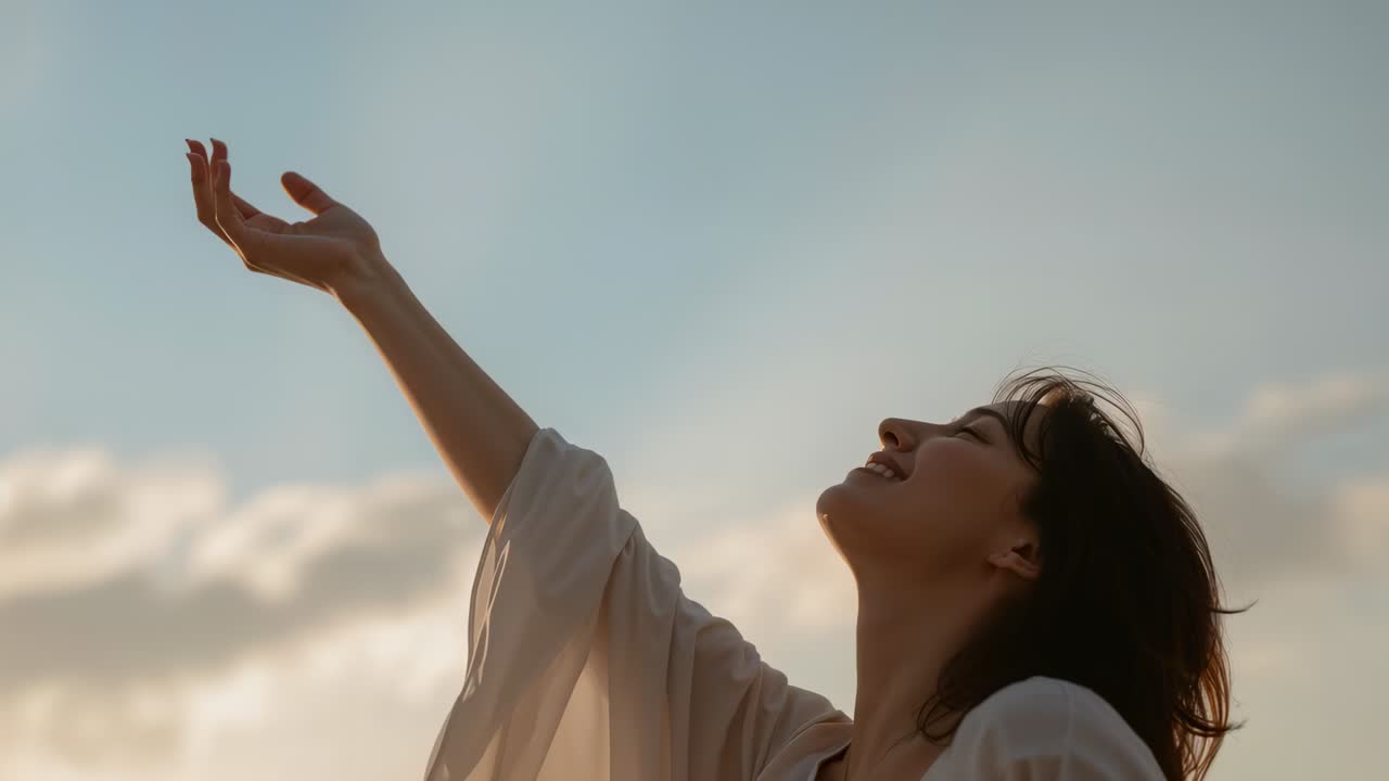 Reaching Asian woman lifting right arm gazing up in golden sky, open hand, blouse, copy space
