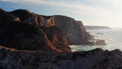 group of hikers hiking on a narrow path with beautiful ocean and coastline cliff view during summer day