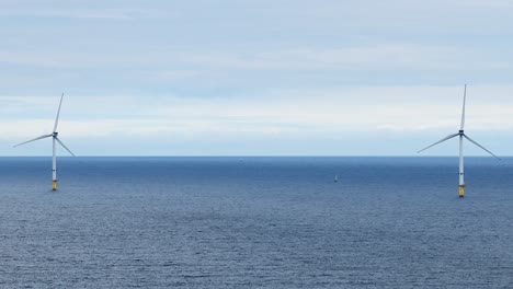 two offshore wind turbines rotate steadily in the open sea under overcast daylight, captured with a static wide shot and minimal camera movement