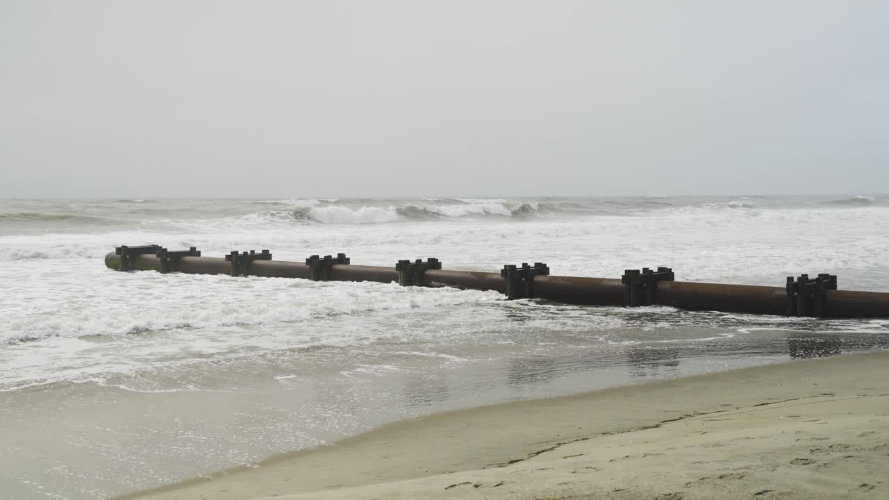 Rough ocean waves hitting drainage pipe on beach on a gloomy day in OCNJ