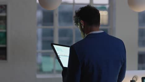 young businessman using tablet computer working late in office browsing financial graph data looking at data statistics on digital touchscreen