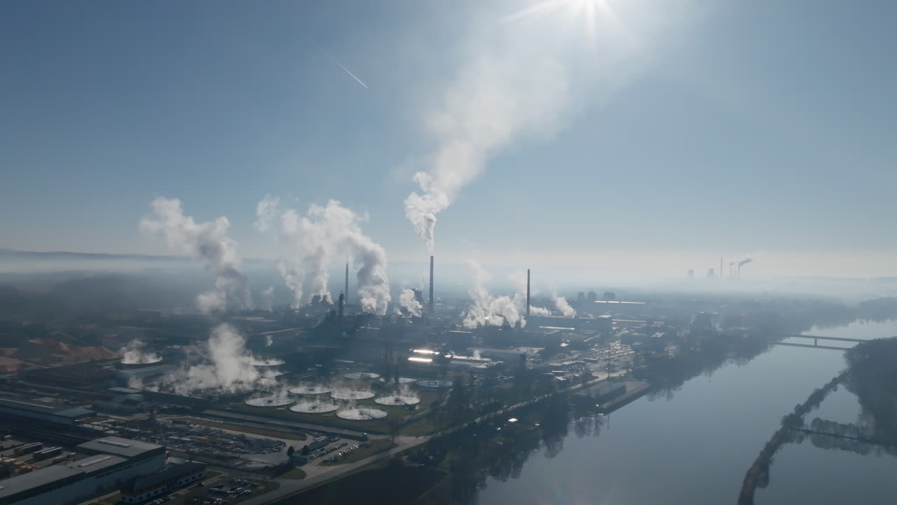 Passaggio ravvicinato di un drone sopra la cartiera di Štětí, che evidenzia gli edifici della fabbrica, le ciminiere che emettono vapore e le fitte reti di tubi, strade e strutture industriali.