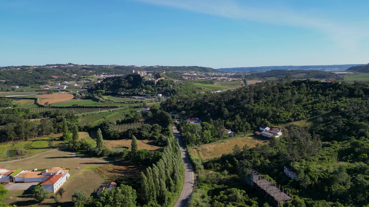 Veduta aerea di un castello storico nel Portogallo centrale, circondato da lussureggianti paesaggi verdi in una giornata di sole, che ne evidenzia la bellezza intramontabile e l'ambiente naturale