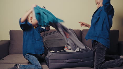 happy brothers taking out clothes from the suitcase and throwing them in the room. joyful boys are making a mess in the room together. slow motion.