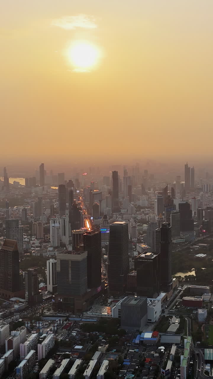 Vista aérea de drone do horizonte da cidade de Bangkok durante o pôr do sol, com luz dourada e quente iluminando a densa paisagem metropolitana. Vertical