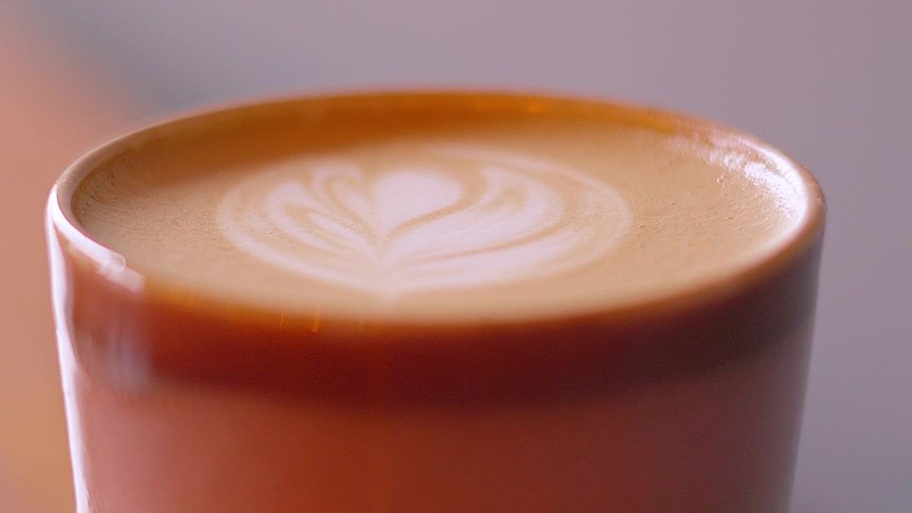 Caffè Flat White appena preparato con latte art schiumato in superficie, sotto una morbida illuminazione naturale. Bevanda calda mattutina di alta qualità e preparata professionalmente.