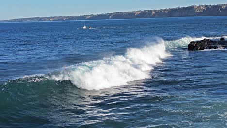 toma de drones de olas rompiendo en el arrecife mientras los leones marinos juegan y el pelícano vuela con un bote en el fondo en la jolla california durante la marea real