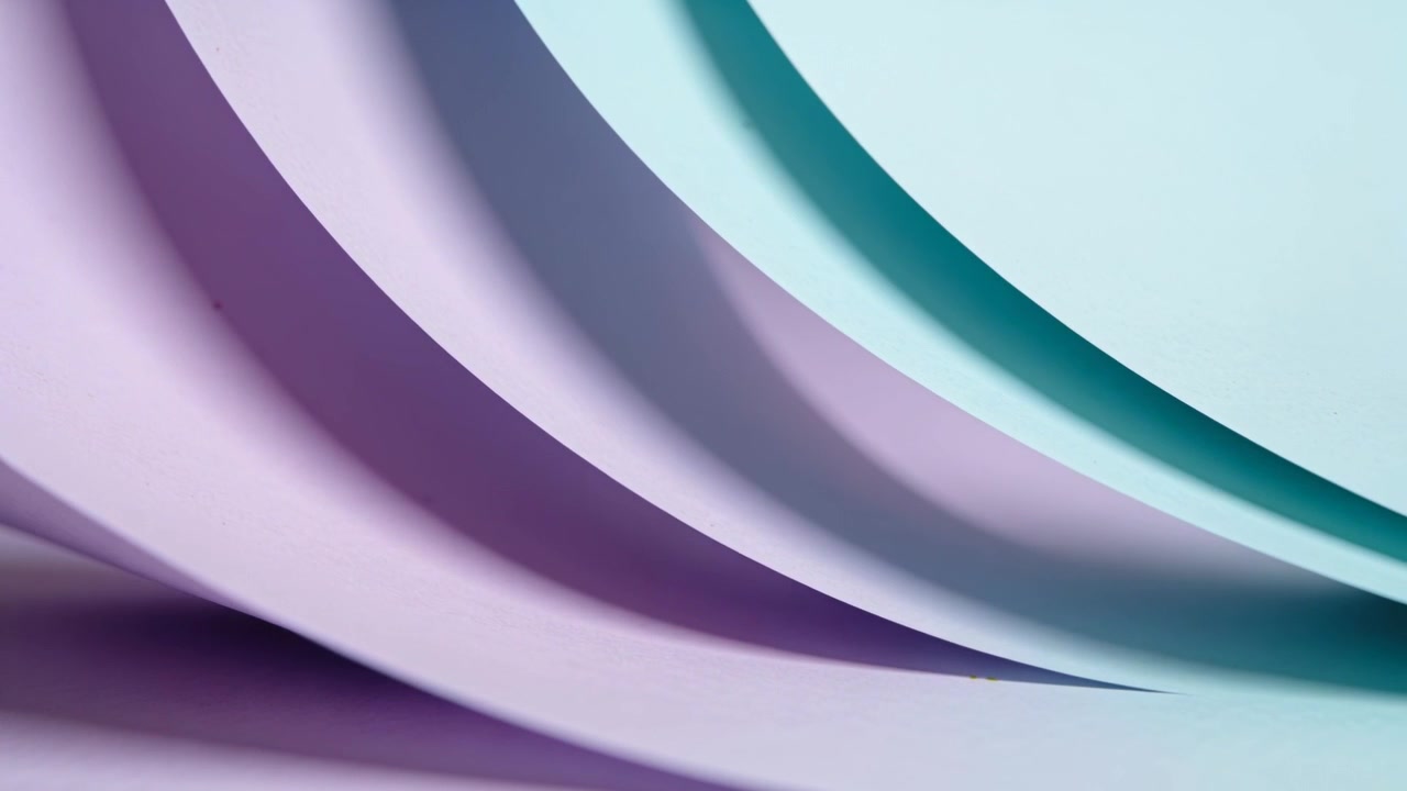 Moving camera revealing lavender and teal curved paper sheets on studio tabletop, enhancing shadows