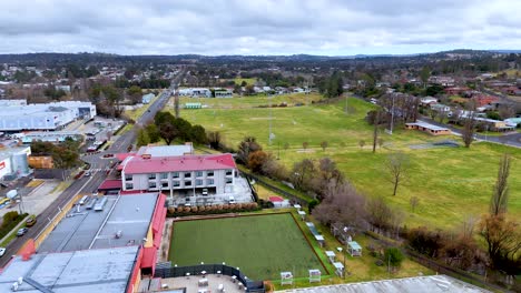 aerial footage shows a drone smoothly flying over suburban armidale, new south wales, revealing green fields, residential buildings, and overcast skies in daylight