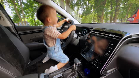 happy little kid sitting on the driver's seat in the car. toddler jumps up excitedly holding by the wheel and touching the panels.