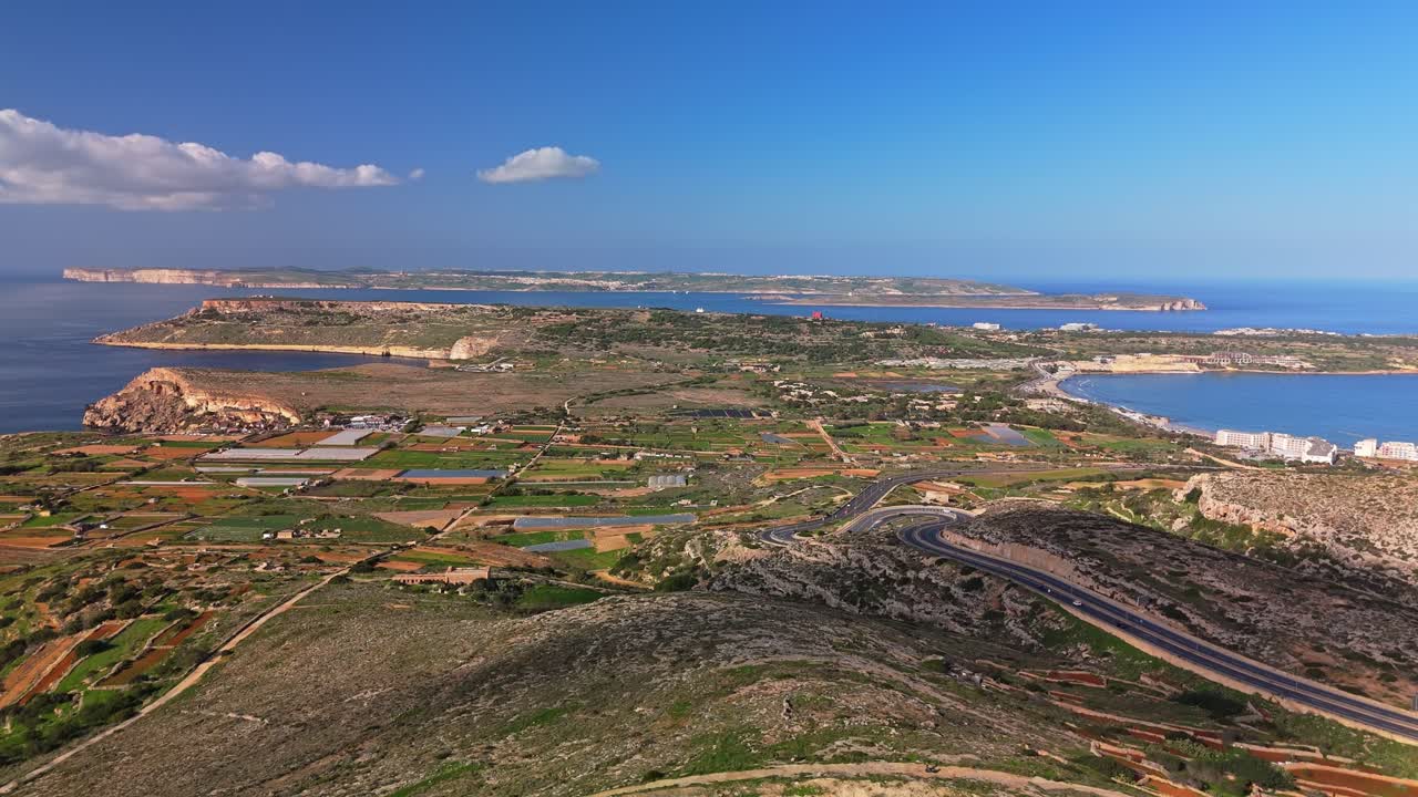 Aerial view of Mellieha, Malta, highlighting agricultural fields, rugged coastal cliffs, and the Mediterranean Sea with Gozo beneath a clear blue sky, capturing the island's scenic and natural beauty