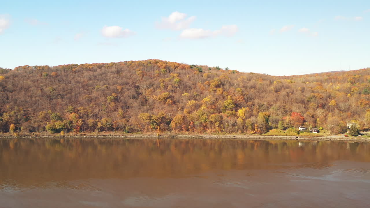 An aerial view over the Hudson River as the drone camera pans right focused on the Mid-Hudson Bridge from Poughkeepsie, NY. It's a bright - sunny fall day - the Hudson River is calm.
