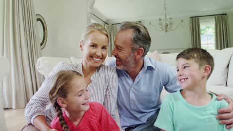 Lächelnde-Familie-Sitzt-Mit-Ausgestrecktem-Arm-Im-Wohnzimmer