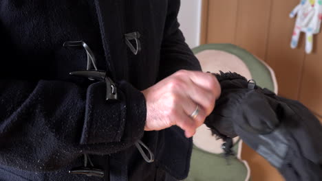 en el día un hombre saca guantes del bolsillo de un abrigo y se los pone en las manos dentro de una casa para salir