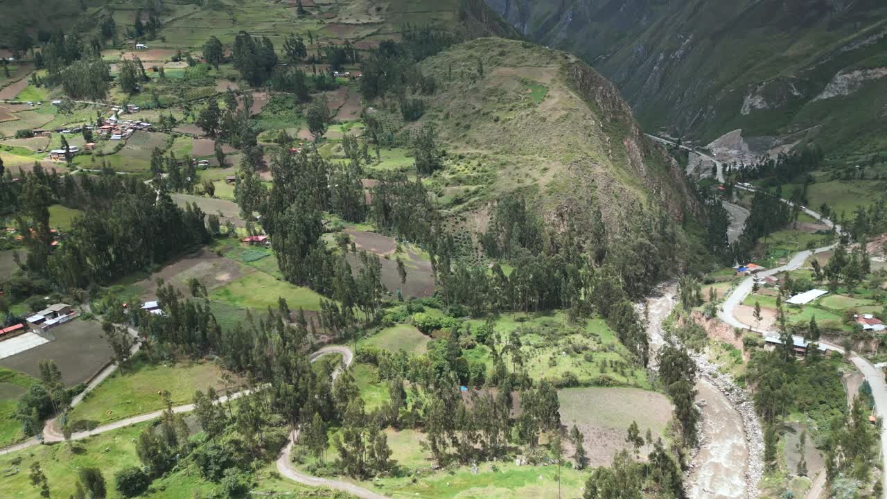 Drone footage of a lush green landscape in Ancash, featuring a river, mountains, and distant houses. The shot captures a unique perspective with a downward movement and upward gimbal.