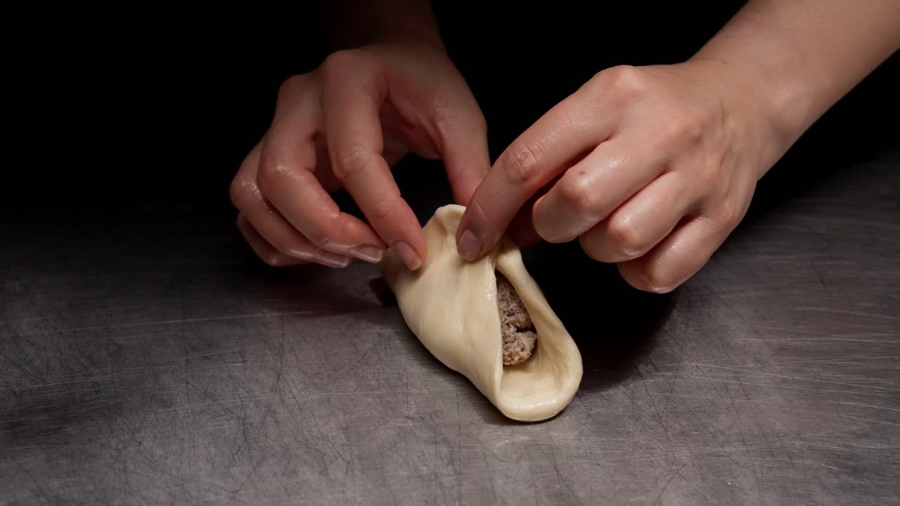 Primo piano di mani che sigillano l'impasto con ripieno di carne