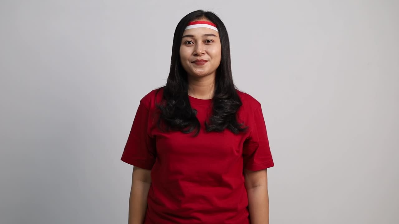 Junge asiatische Frau, die seitlich und in die Kamera salutiert und den indonesischen Unabhängigkeitstag am 17. August feiert.