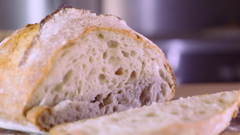 Hand-Moves-A-Slice-Of-Sourdough-Bread-On-A-Wooden-Board---macro,-pan-shot