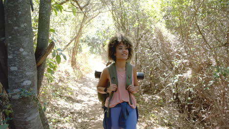 young biracial woman hikes on a sunny trail, sporting a backpack