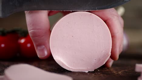 male hand with a knife cut boiled sausage into round pieces.