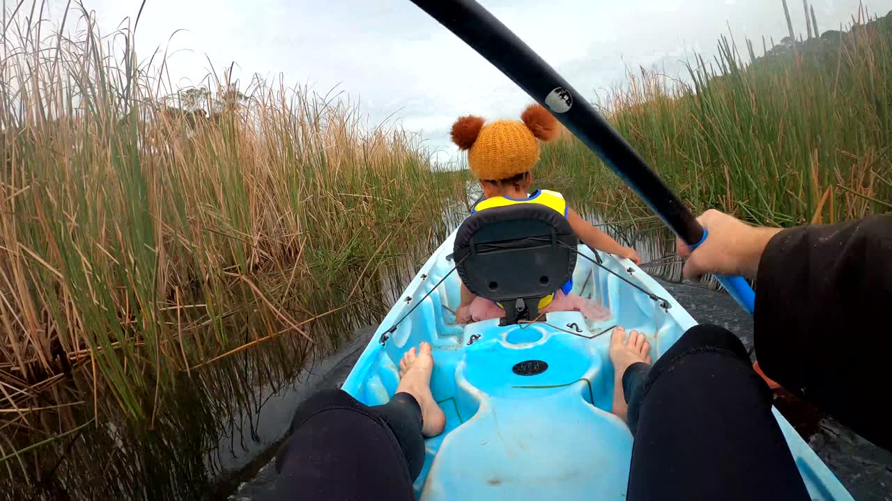 Point of view shot of a man paddling very fast on a lake in a tandem kayak with his daughter in the front.