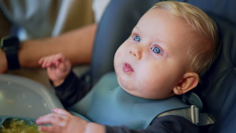 adorable blond caucasian baby chewing food. cute portrait of a kid in a bib fed from a spoon.