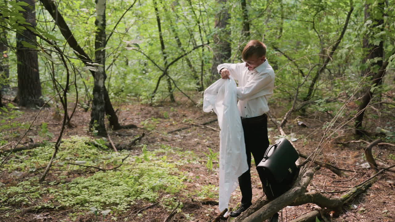 Scientific researcher in white shirt carefully putting on white coat in forest near black leather bag on tree branch, surrounded by woodland greenery, branches, and natural sunlight