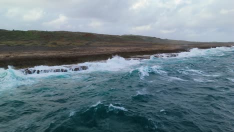 Vuelo-Aéreo-En-ángulo-A-Lo-Largo-De-La-Costa-Con-Fuerte-Oleaje-Rompiendo-Olas-Contra-Rocas-Afiladas