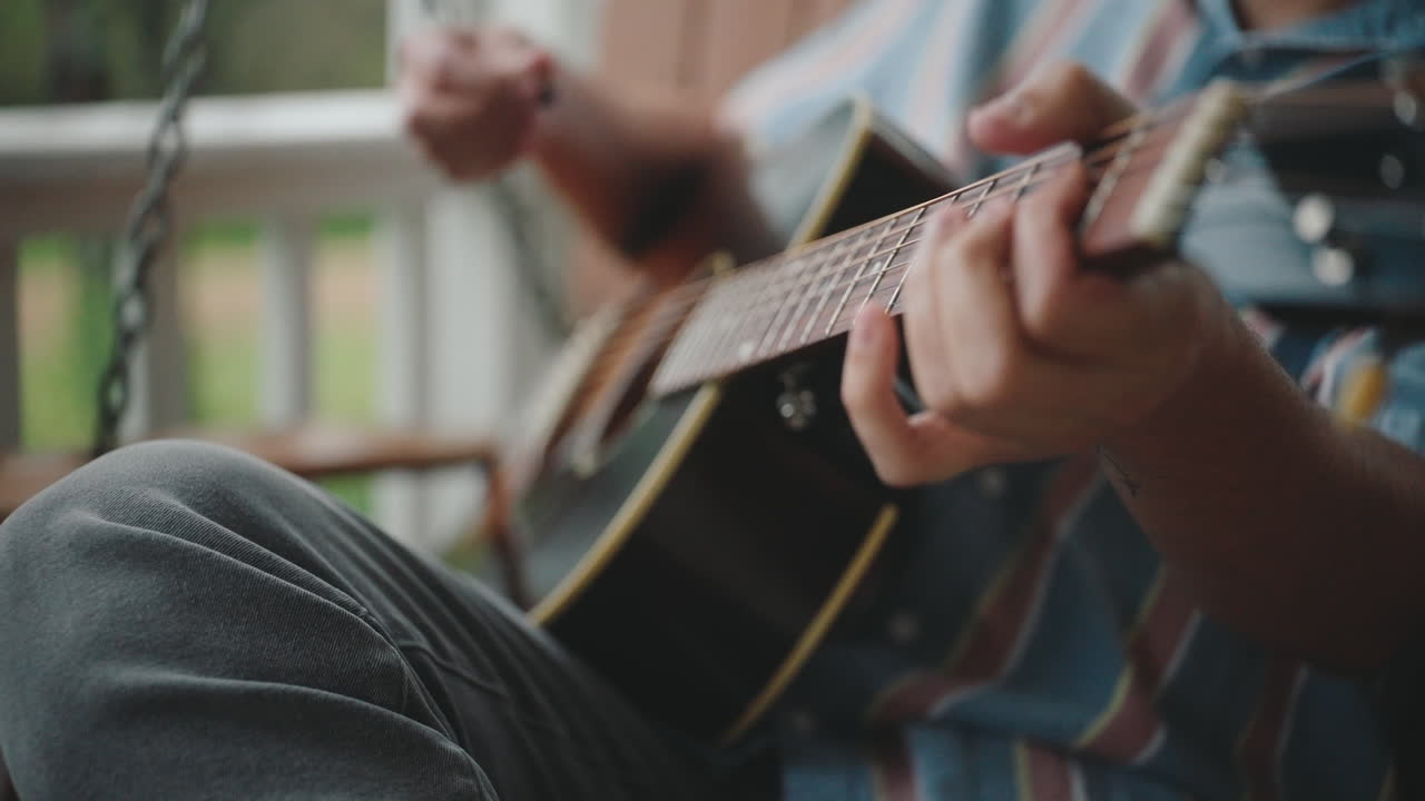 Man playing acoustic guitar on a porch swing