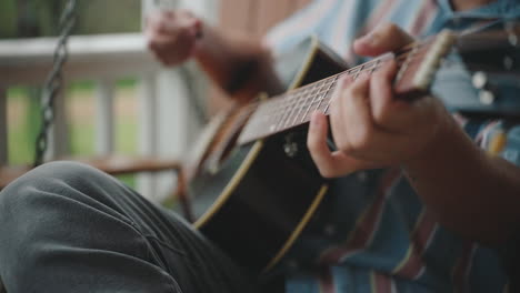 man playing acoustic guitar on a porch swing