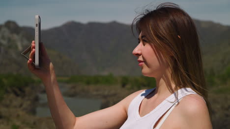 mujer feliz hace selfie contra las montañas y el río