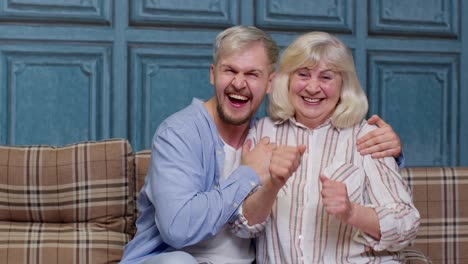 generations family of senior mother and handsome adult son or grandson dancing together, laughing