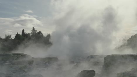 Geothermal-geyser-Erupting-with-steam-and-water,-Rotorua,-New-Zealand,-Slow-motion-natural-iconic-steamy-rocky-environment,-Sunny-Daytime-Sky