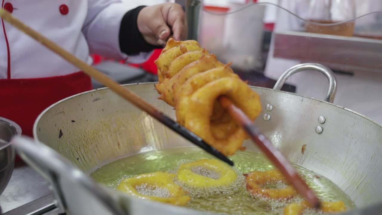 Chef che frigge frittelle dorate a forma di anello nell'olio bollente