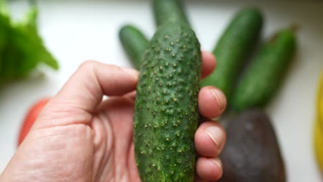 mano sosteniendo un pepino fresco con otras verduras