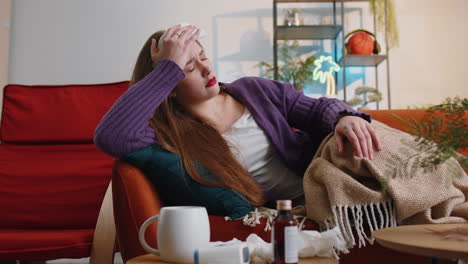 sick ill young woman suffering from cold allergy lying on home sofa sneezes wipes snot into napkin