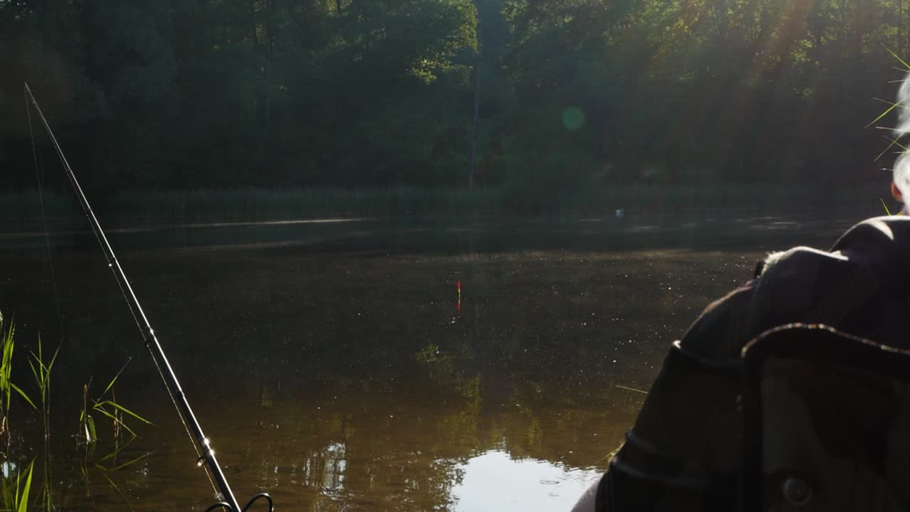 Fischer angelt auf dem See, während er raucht, wobei weißer Rauch von der rechten Seite des Videos aufsteigt