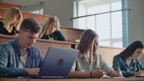 Eine-Große-Gruppe-Multiethnischer-Studenten-Arbeitet-An-Ihren-Laptops,-Während-Sie-Im-Modernen-Klassenzimmer-Einer-Vorlesung-Lauschen.-Kluge-Junge-Leute-Studieren-An-Der-Universität.