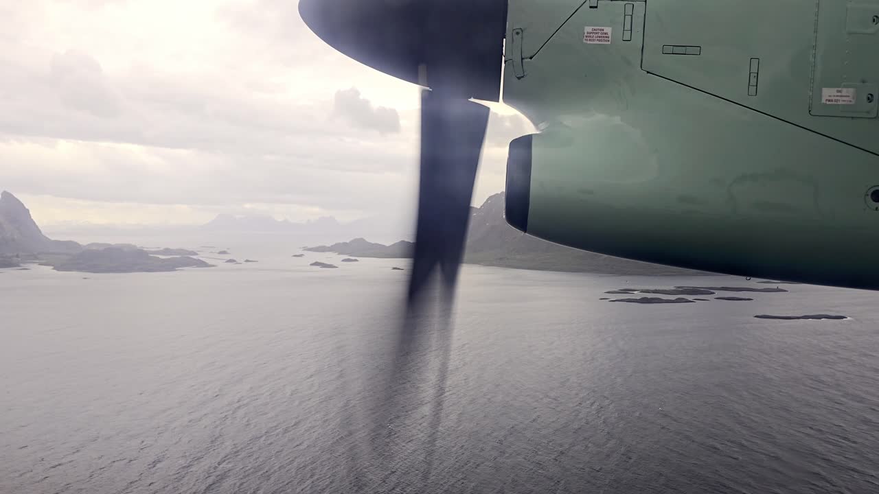 Window view from Wideroe propeller airplane cruising at low altitude over sea beside Lofoten mountains