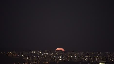 la súper luna llena que se levanta sobre la ciudad nocturna.