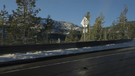 trees and road signs pass by as seen from the road in front of a mountain landscape in lake tahoe