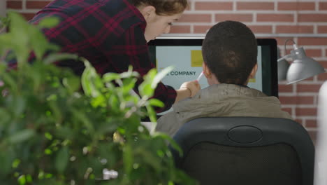 young caucasian team leader woman training african american intern pointing at computer screen sharing ideas showing support helping student in diverse modern office