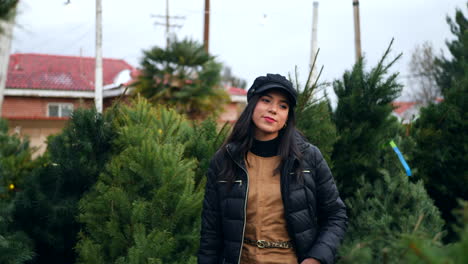 una mujer hermosa con un espíritu navideño feliz sonriendo mientras compra árboles de navidad festivos de abeto douglas