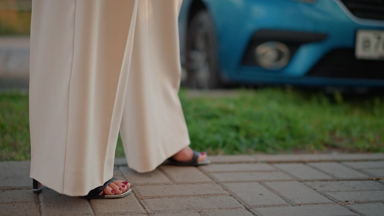 Beskåret lavvinkelbillede af en person, der går langs et brolagt fortov iført beige vidde bukser og sandaler med åben tå.
