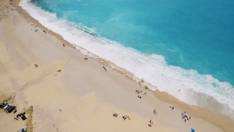 Myrtos-beach-with-turquoise-waters-and-scattered-sunbathers-on-sand,-kefalonia,-greece,-aerial-view