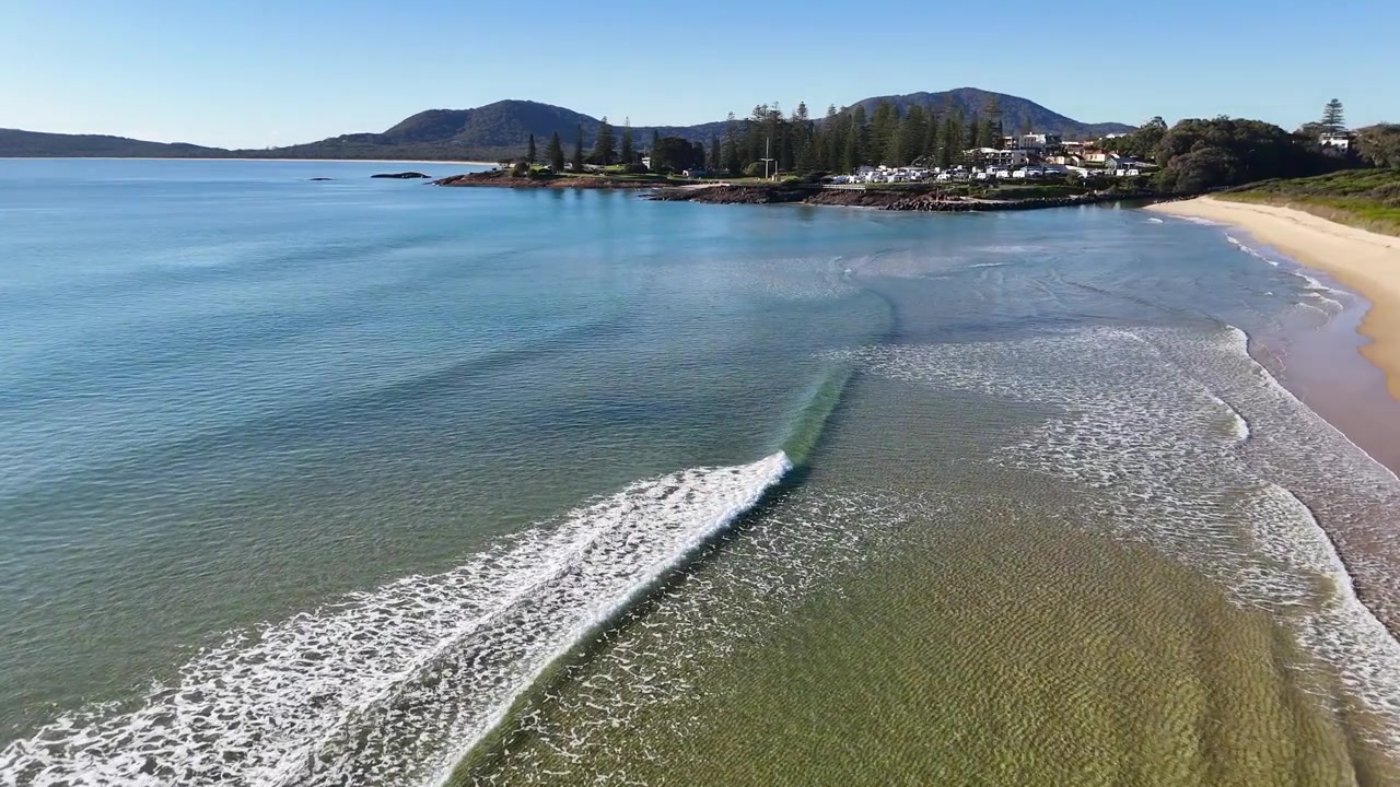 Høytliggende dronebilde av turkise bølger som bryter på en sandstrand i Australia
