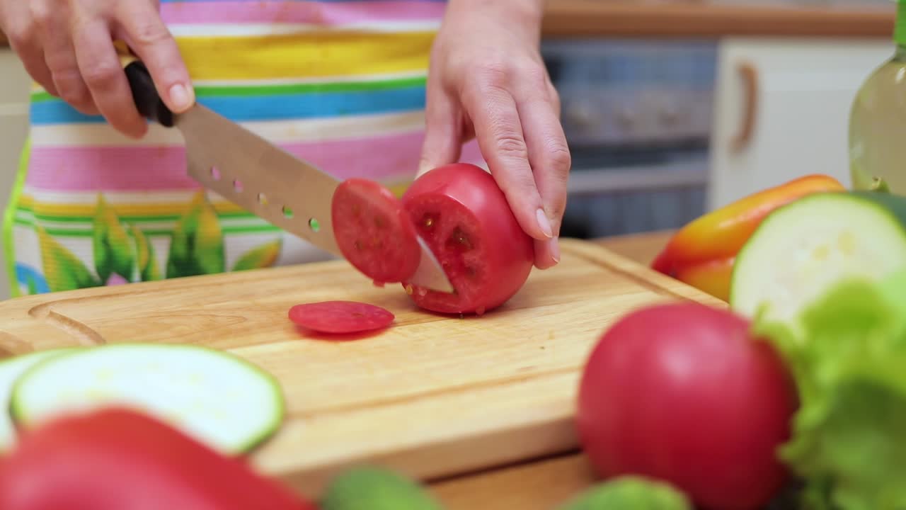 Women's hands Housewives cut with a knife fresh tomato on the cutting Board of the kitchen table