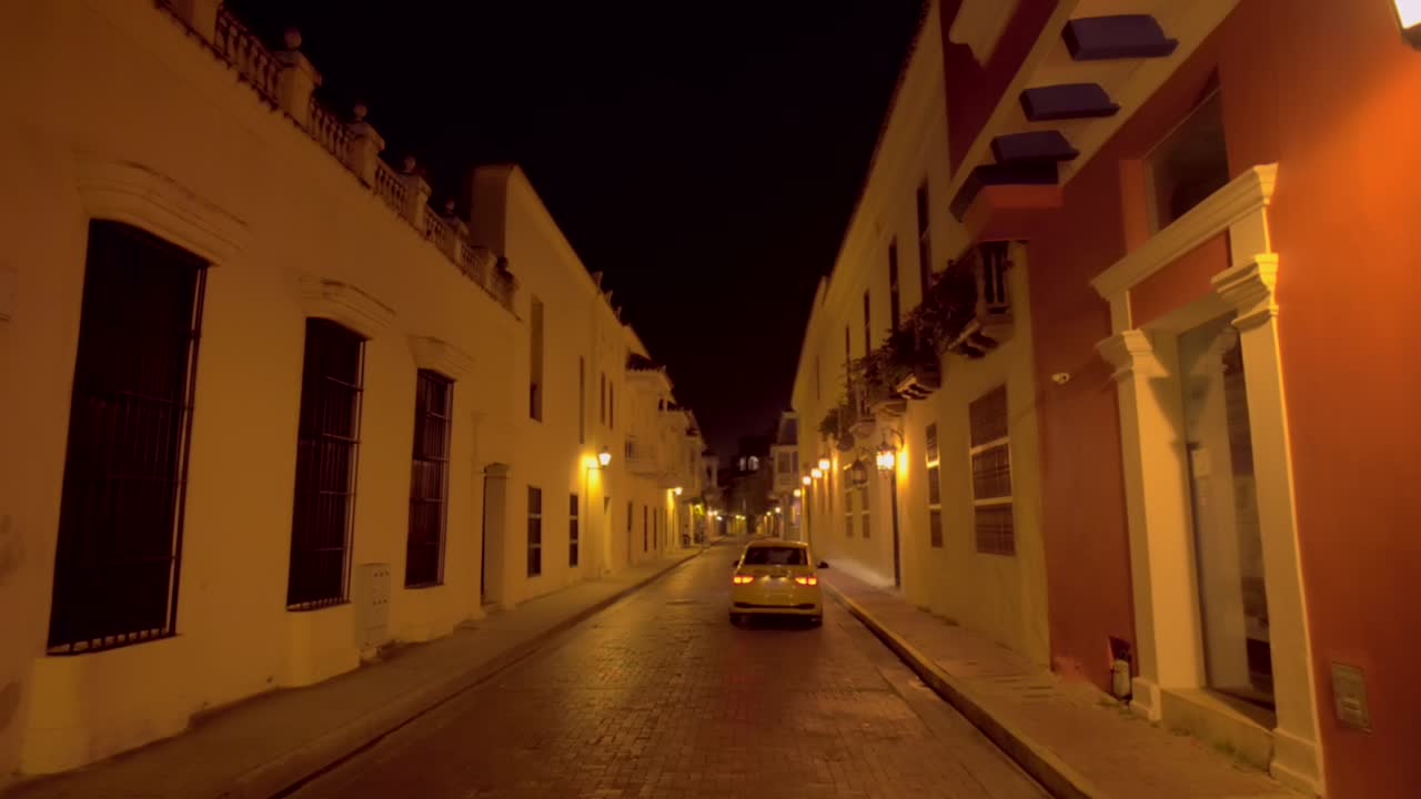 Romantic and mysterius shot of a colonial street in Cartagena Colombia by night, while a taxi turns left and transits the street