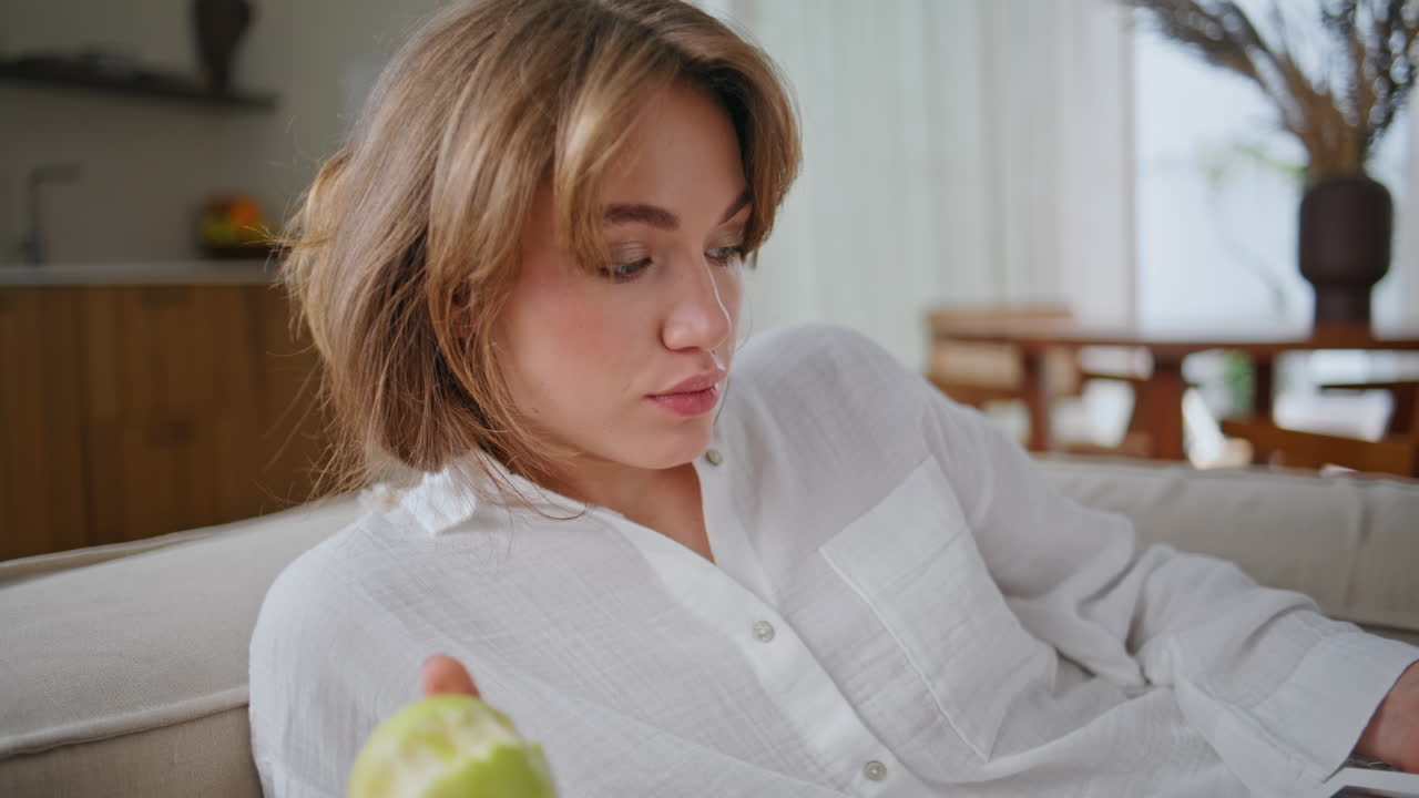 Lazy girl relaxing sofa chewing green apple at domestic weekend morning closeup