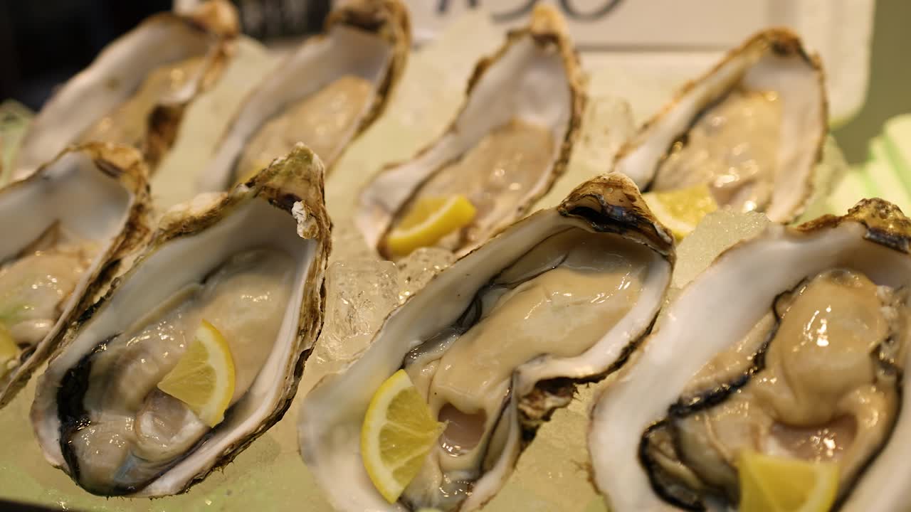 Close-up panning shot of fresh raw oysters served with lemon on ice at Kuromon Market